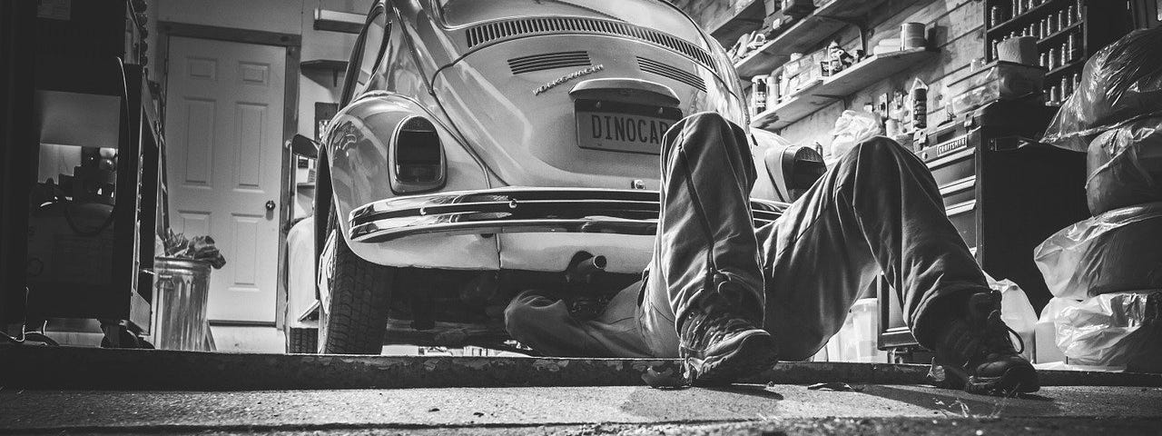IMAGE: In black and white, an auto mechanic crawling under a Volkswagen Beetle
