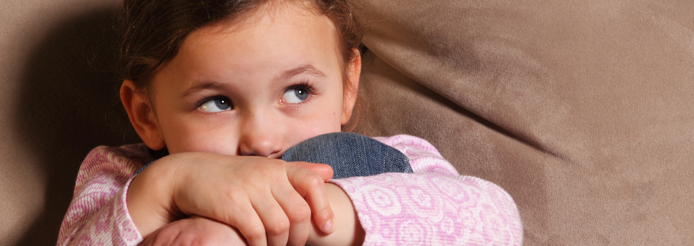 Little girl sitting on a sofa, looking sad or scared.