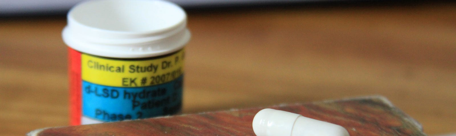 A white pill on top of a wodden box with a prescription bottle behind it. Photo courtesy of the Multidisciplinary Association for Psychedelic Studies