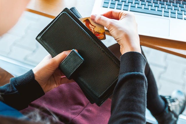 A woman pulling out her credit card from her wallet while sitting at a table in front of an open laptop