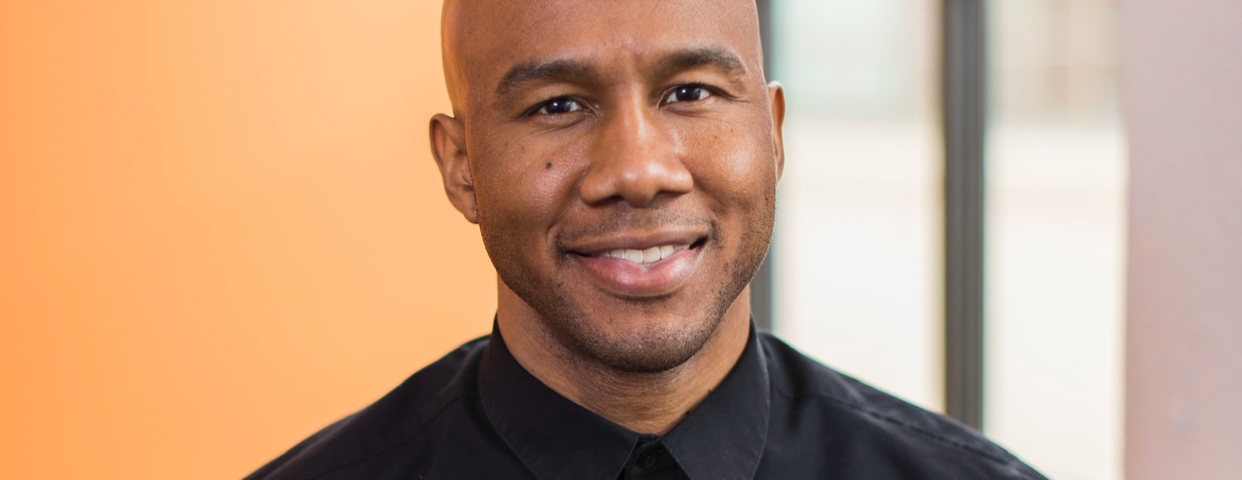 Javier, a bald Black man, wears a black button down shirt and is smiling with teeth visible.