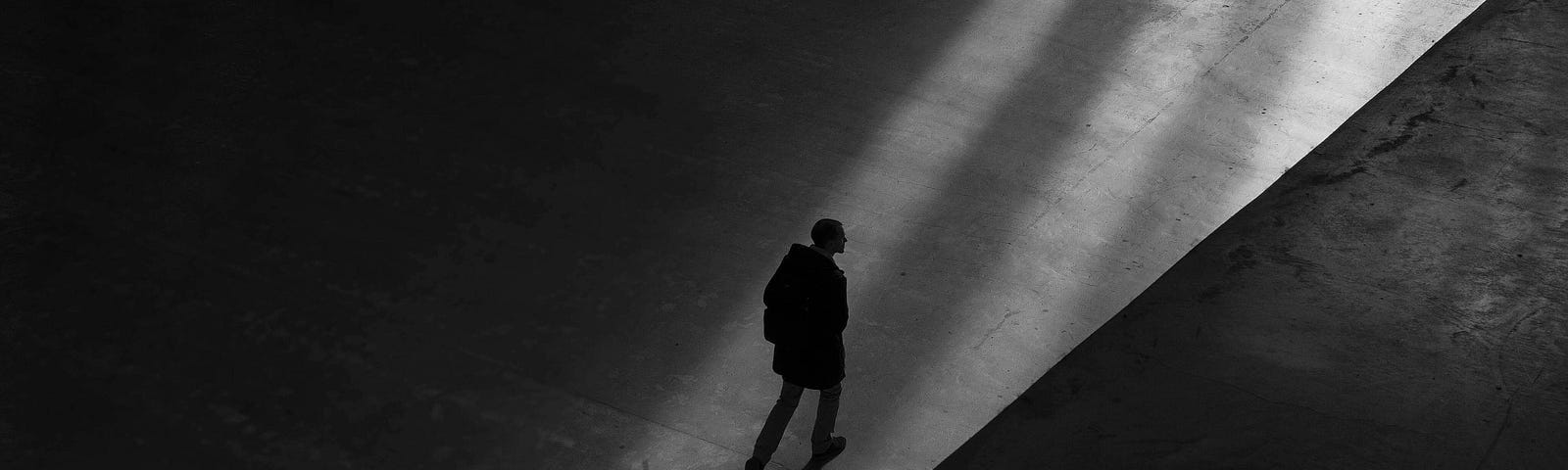 A person walking in the light amidst the shadows.