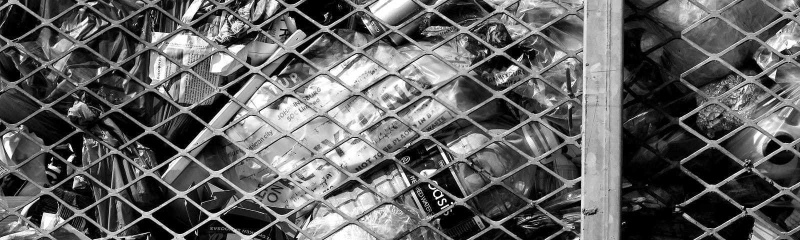 Monochrome photo of garbage pressed against a chainlink fence