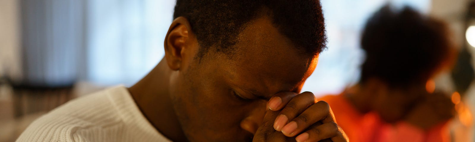 A young Black couple sit apart on the couch with their heads resting sadly in their hands.