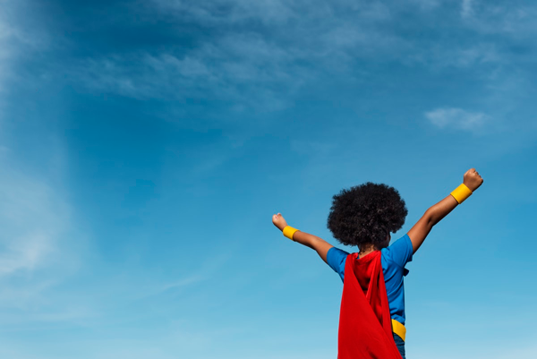 Child dressed as a superhero, triumphantly raising arms