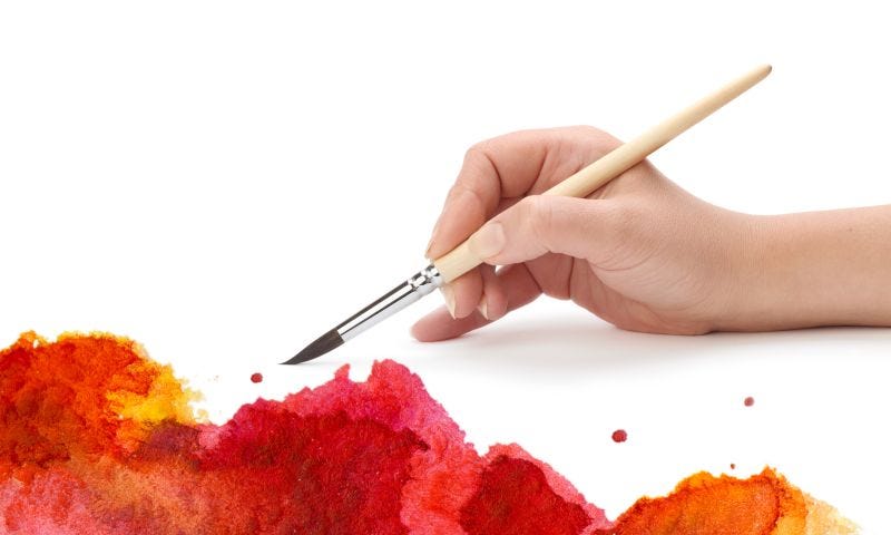 A hand with a brush painting in red, orange and yellow colours