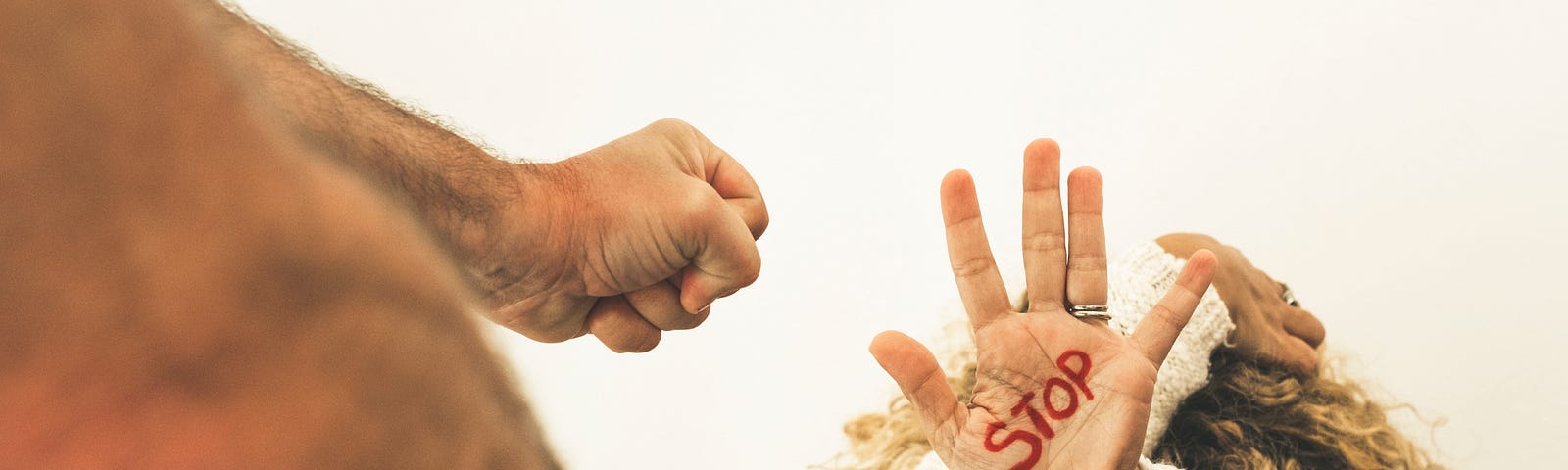 A woman cowers in fear from domestic violence with the word “stop” written on her hand.