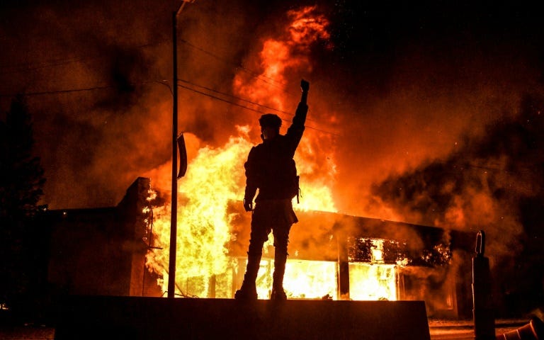 A protester raises a clenched fist in front of a burning building in Minneapolis. (AFP Photo)