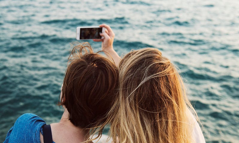 Two people holding a phone as if taking a photo together, viewed from behind