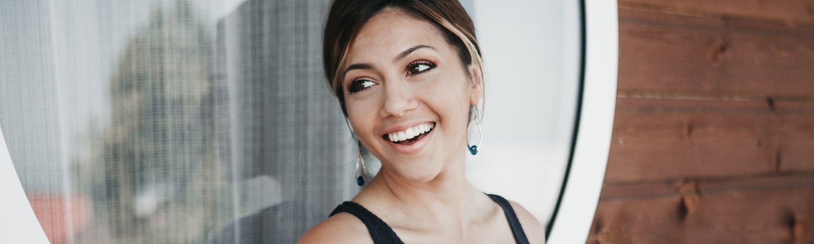 A person smiling with coffee by a window.