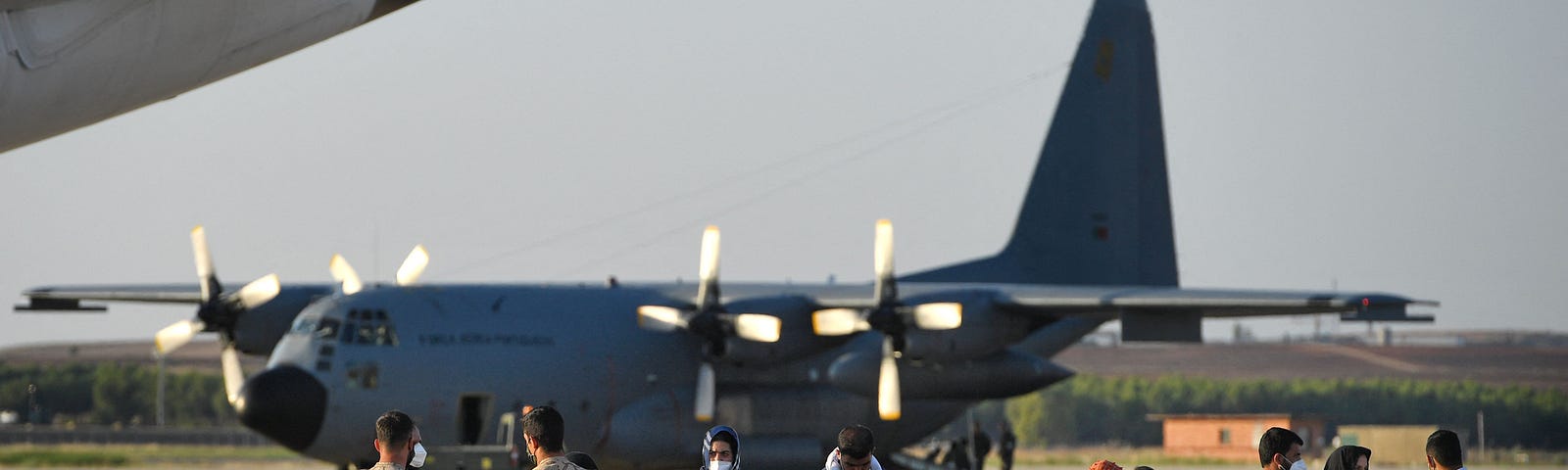 A group of Afghan refugees wait on the tarmac next to a large transport plane after being evacuated to Madrid, Spain.