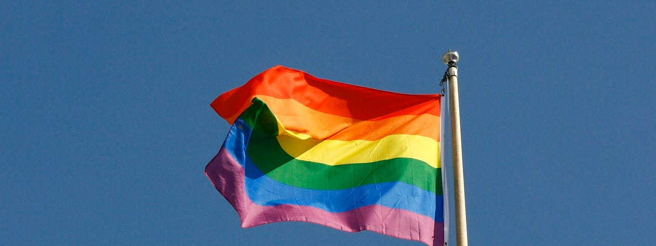 The rainbow flag which represents Pride flying against a blue sky