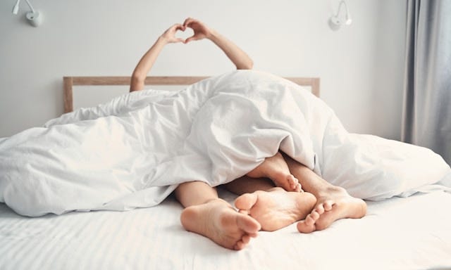 Couple in bed, making heart sign with their hands