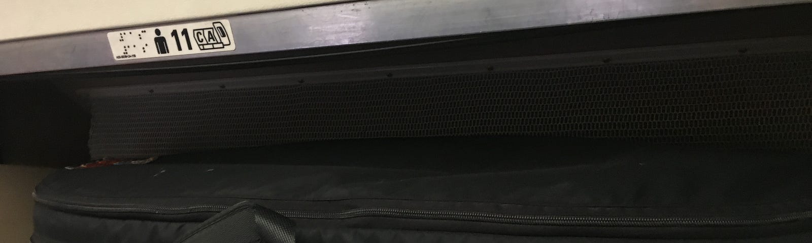 An instrument case inside an overhead bin on an airplane.