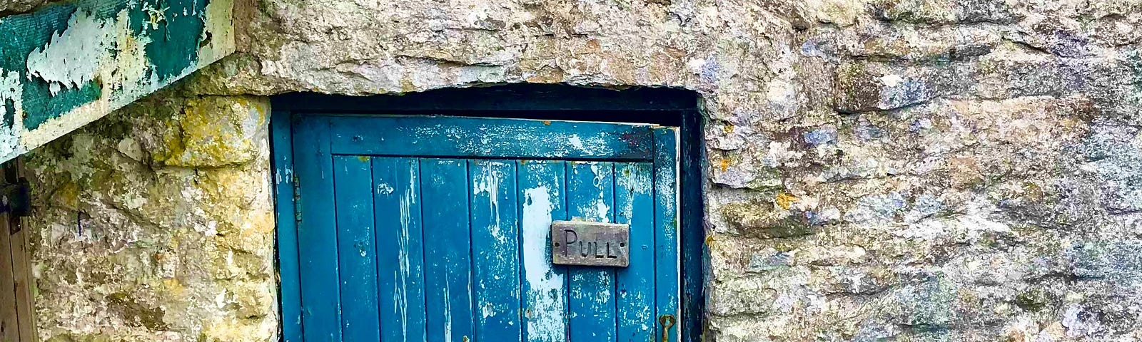 A small door nestled within a stone wall. There is a small sign which reads: “Pull”.