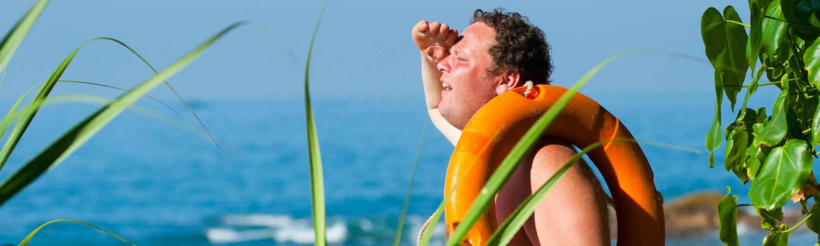 Man looking out over ocean with life preserver on his shoulder