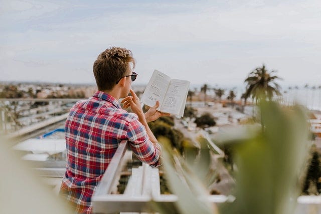 A guy reading a book at a balcony with a view