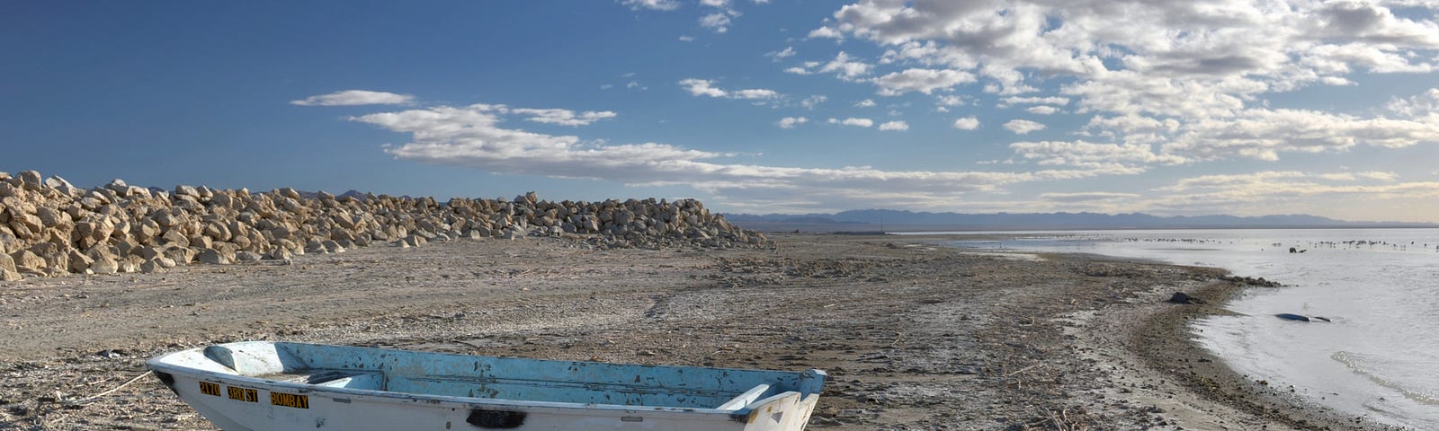 A rundown boat beached on the rocky, fish covered shores of the Salton Sea.