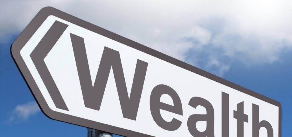 Black on White arrow-shaped sign reading “Wealth” against a blue sky with white clouds.