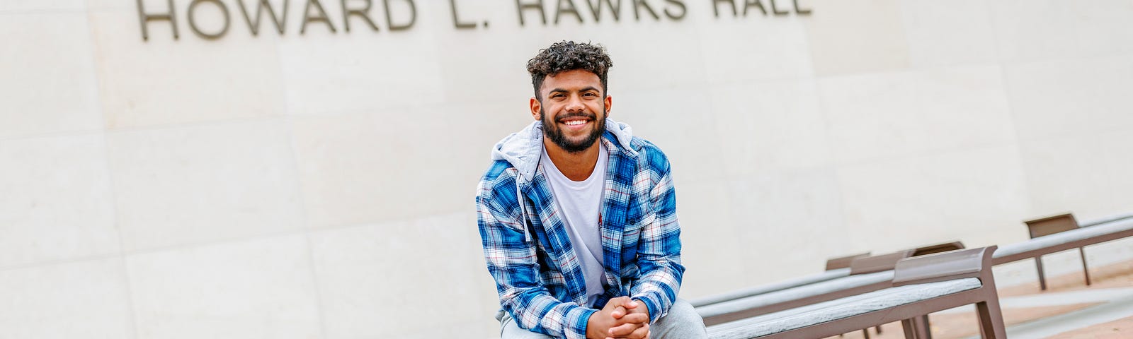 Derek smiles for a photo on the benches outside of Hawks Hall