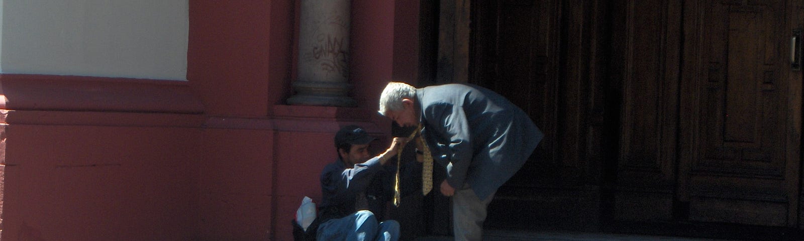 older man bends over to help a man prone on the steps of a church in Santiago Chile