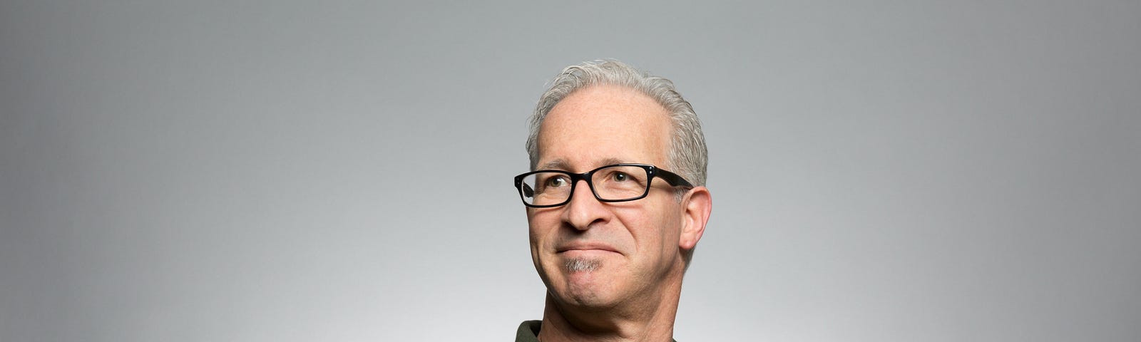 A head and shoulders shot of a white man with greying hair and glasses standing tall and looking somewhat proud of himself.