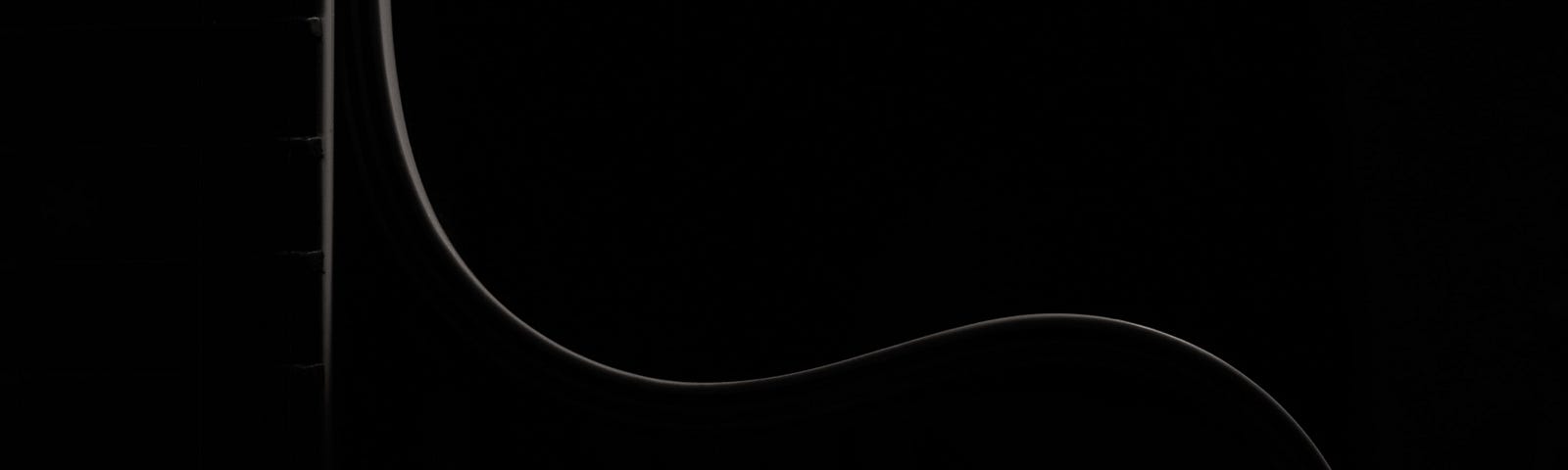 Photo of upright guitar outlined by a sliver of silhouetted light on the neck and upper body in complete darkness.