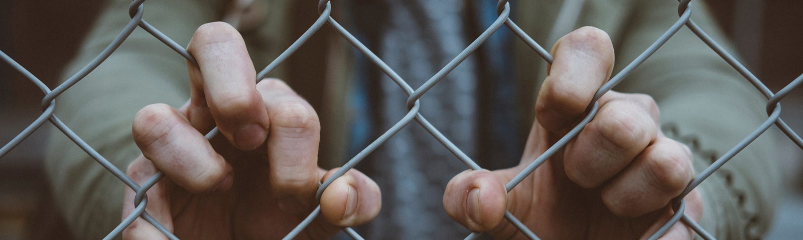 Close-up of a man’s hands grabbing a wire fence.