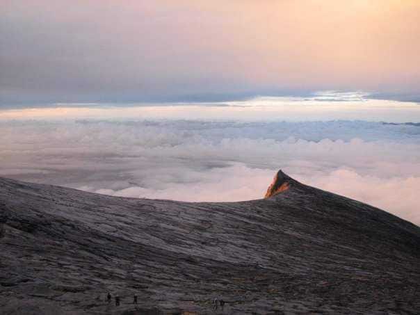 A long rock ridge leads to a view of pink, hazy, cloud cover