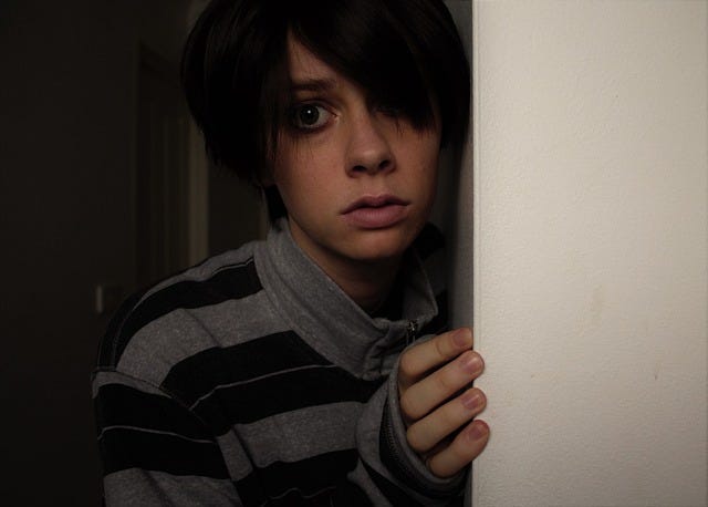 Photo of a scared or anxious young person peeking around the corner
