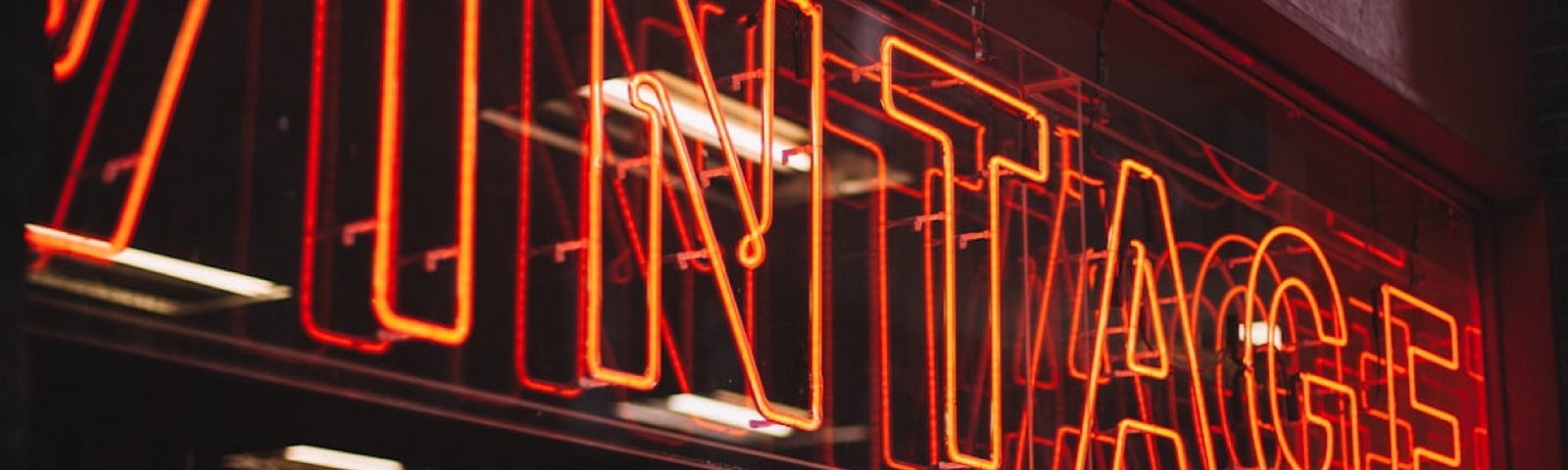 An orange neon sign on a black wall, reading “Vintage”