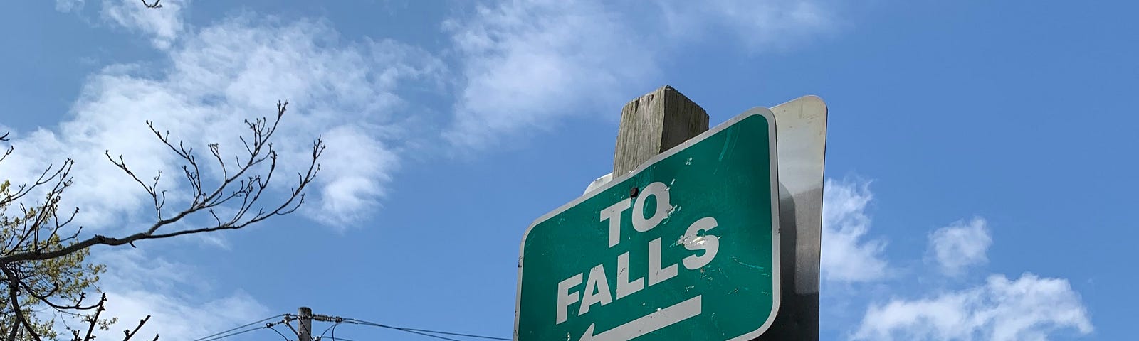 A sign in front of a blue sky reads “TO FALLS” with an arrow pointing left.
