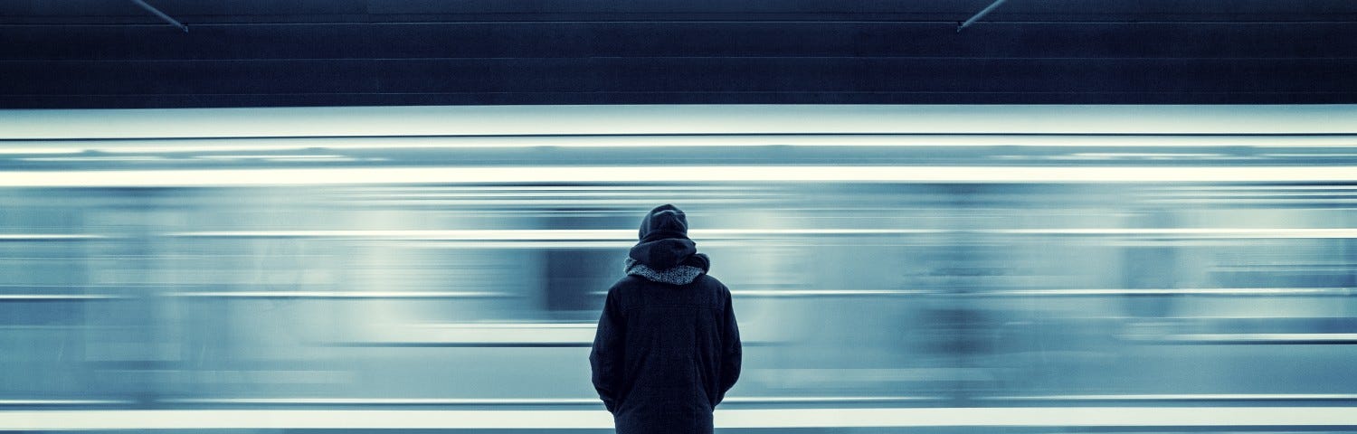 A person stands alone on a platform as a subway train whizzes by in a blur.