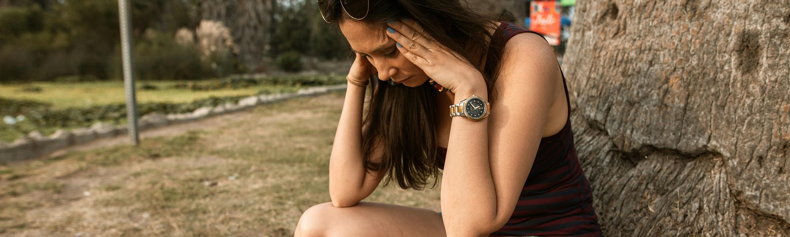 breakups, woman holding her head and looking distressed while crouching by a wall in a field