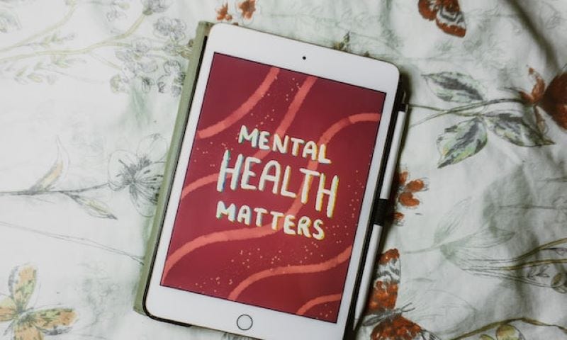 An iPad with a graphic that reads, “Mental Health Matters” with a red and light red wavy background. The iPad is laying on what appears to be a bedsheet with butterflies and flowers.