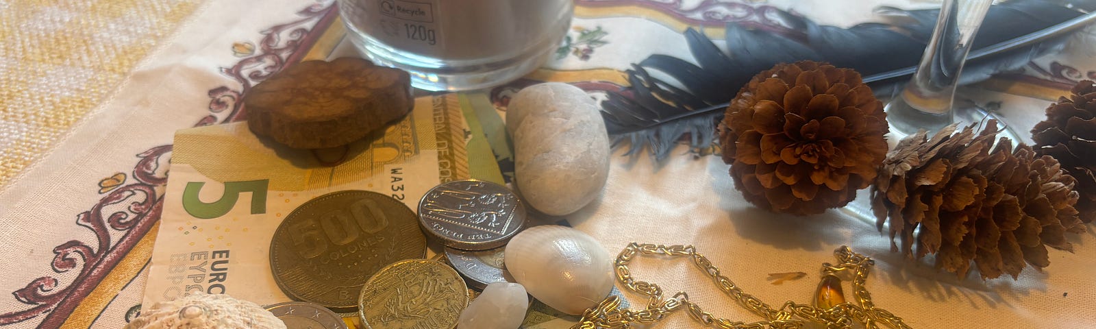 Currency among shells, crystals, jewels, tiny pine cones, a feather and a candle, representing abundance and freedom on the altar.