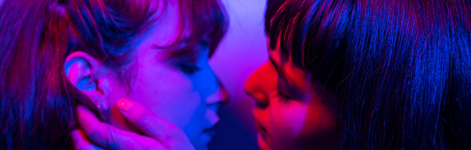 two young women in an embrace under blue light