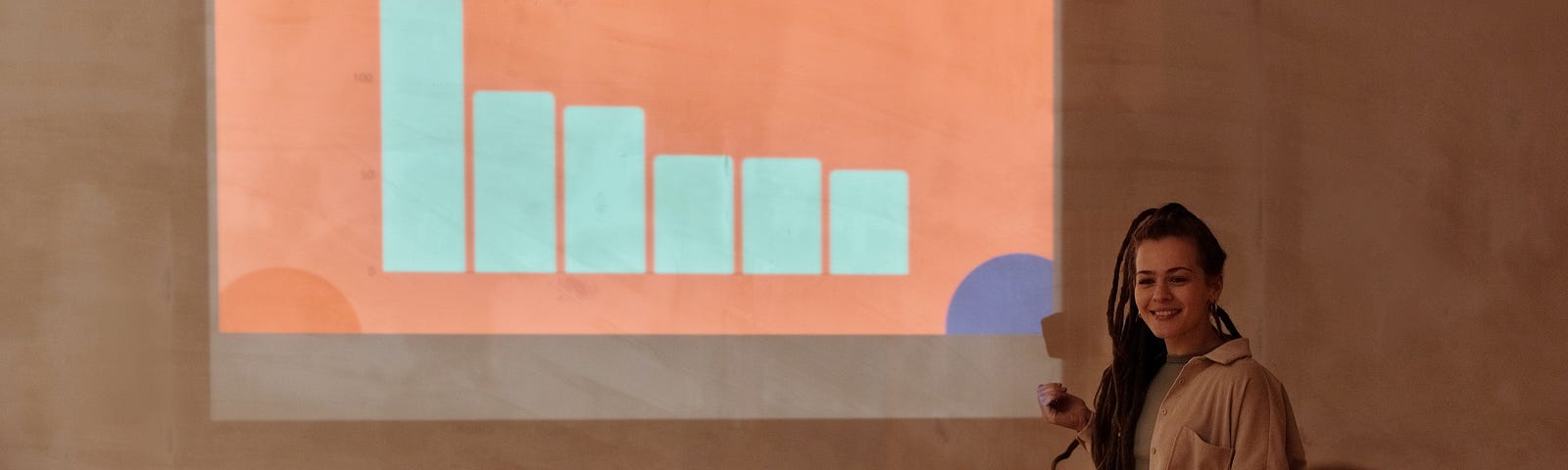 A presenter stands in front of a projected PowerPoint bar chart