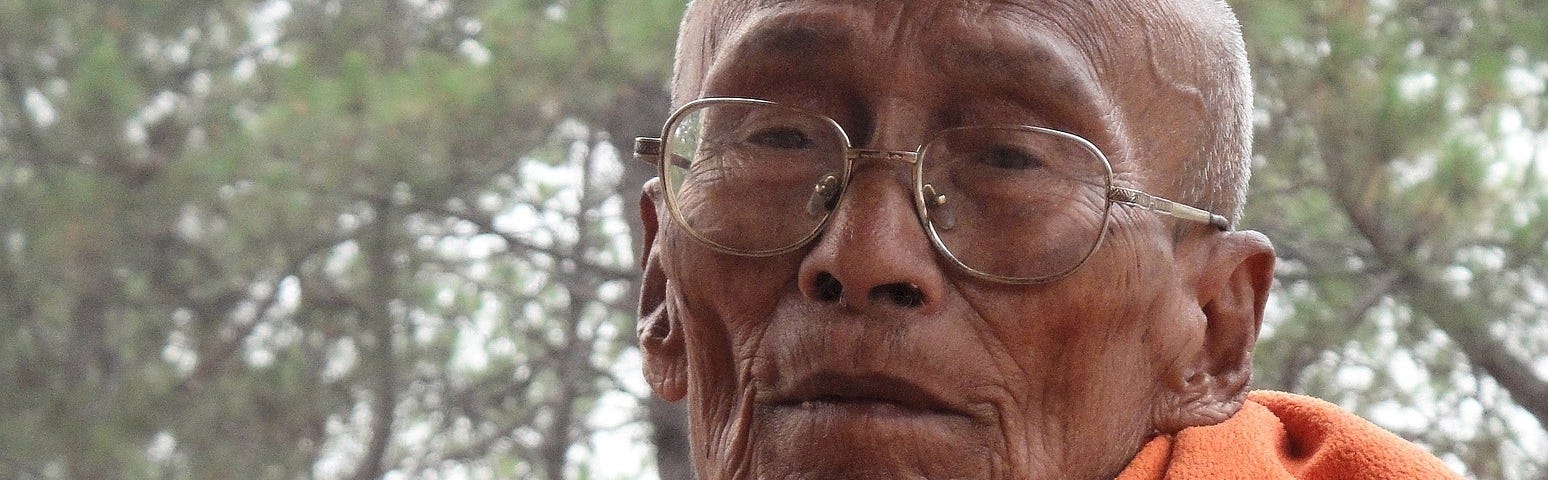 Picture of an old Buddhist monk with weathered face and an orange robe draped over his shoulder