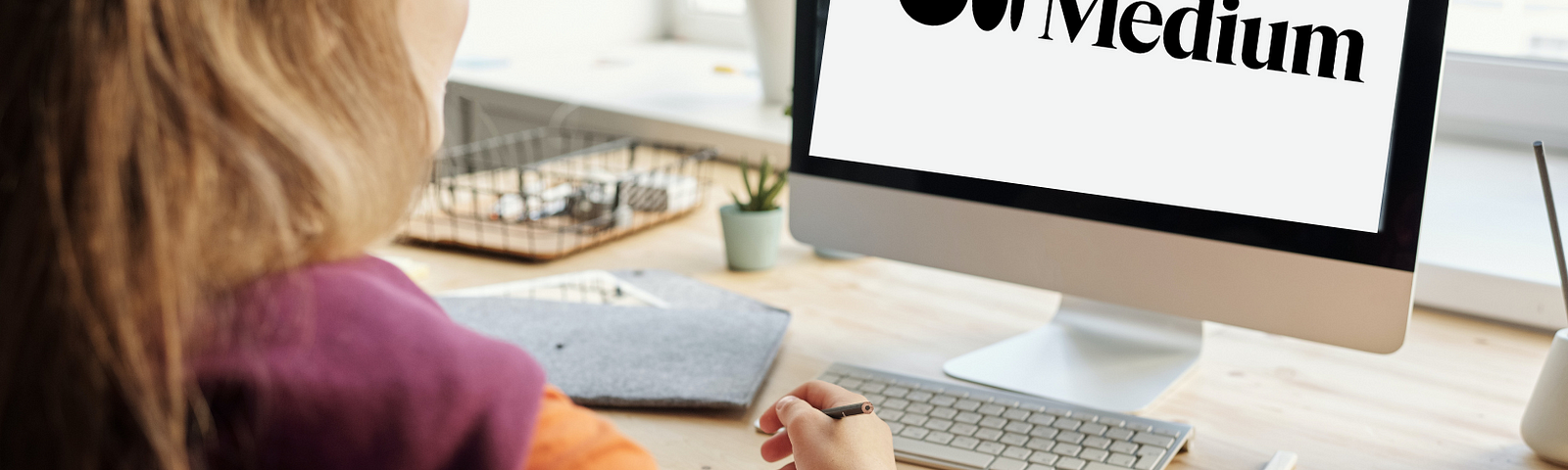 A woman sitting at a desk, looking at a computer screen that says ‘Medium’ on, about to start writing.