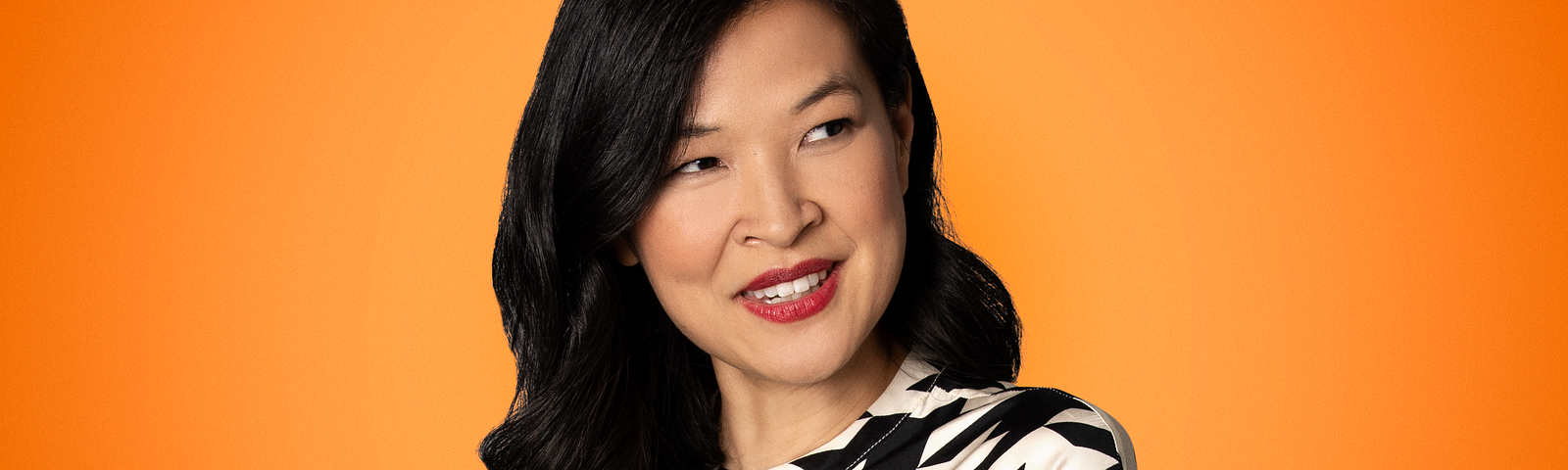 A photo of journalist, author and podcaster SuChin Pak with an orange background