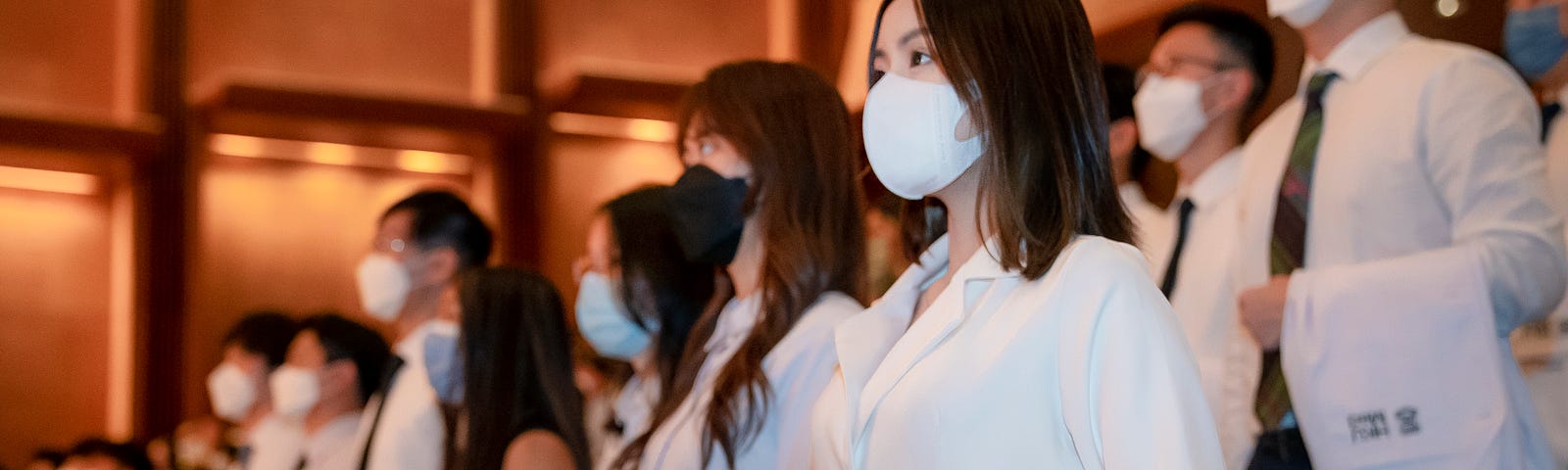 Students stand in rows with their white coats over their arms