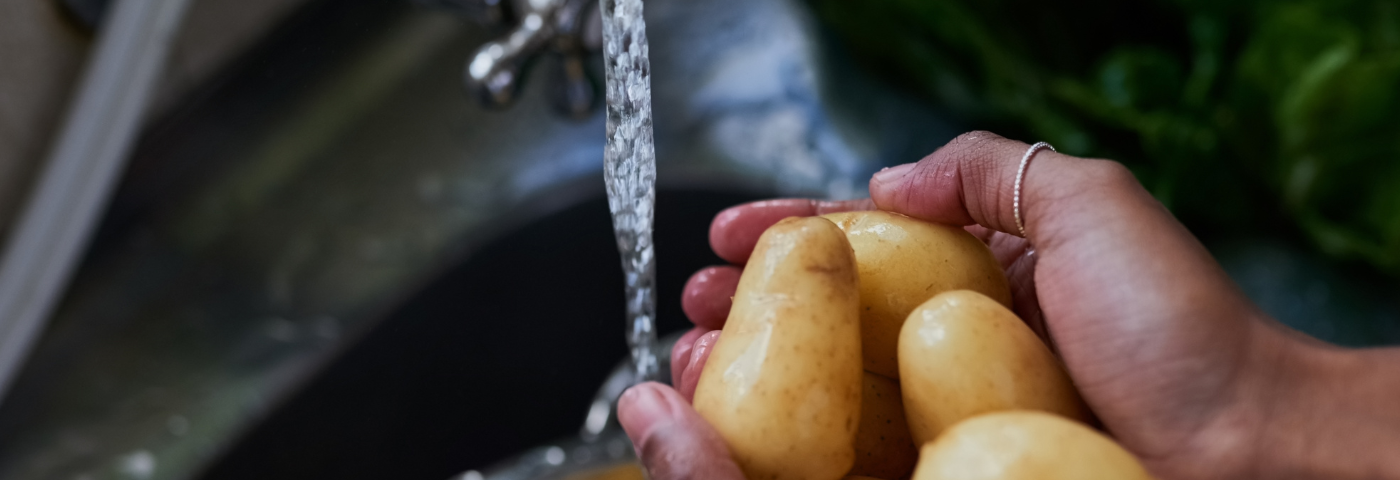 A person washing a handful of golden russet potatoes under running water in a sink