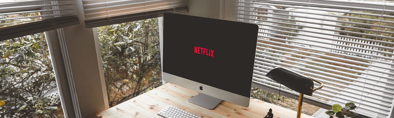 A desk in front of a window with a computer displaying Netflix, a lamp, and a mug