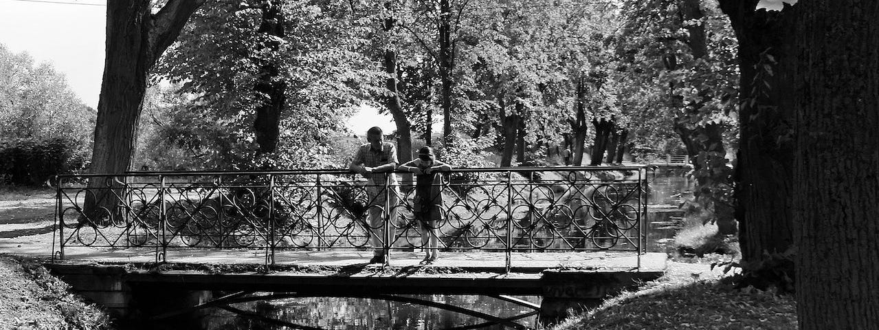 A black and white photo of a father and his daughter standing on a bridge.