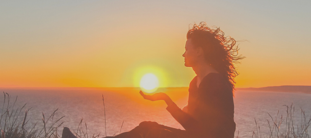 Young woman holding sunset in her palm