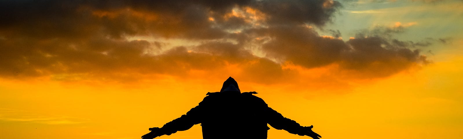 A man standing with arms outstretched, head back, in front of a beautiful sunset