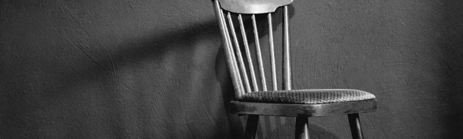 Empty small wooden chair against plain wall.