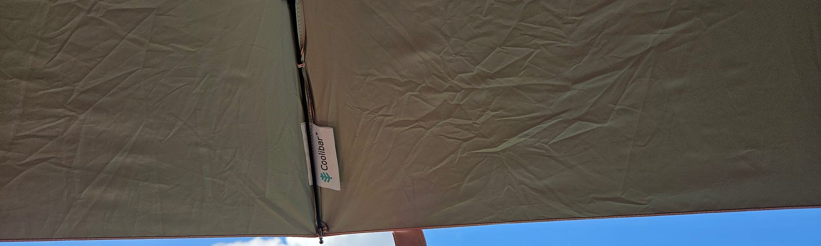 Behind a grey pink parasol, a vibrant blue sky with whispy clouds