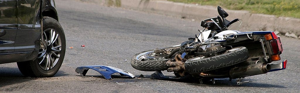 A motorcycle lying on its side on a paved road, with visible cosmetic damage.